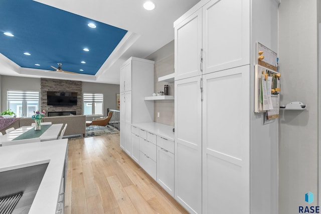 kitchen featuring light hardwood / wood-style floors, white cabinets, a fireplace, and a tray ceiling