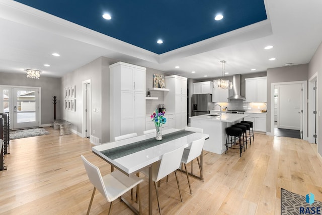 dining room featuring sink, a notable chandelier, a tray ceiling, french doors, and light wood-type flooring