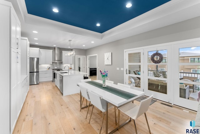 dining area featuring sink, a chandelier, light hardwood / wood-style floors, a raised ceiling, and crown molding