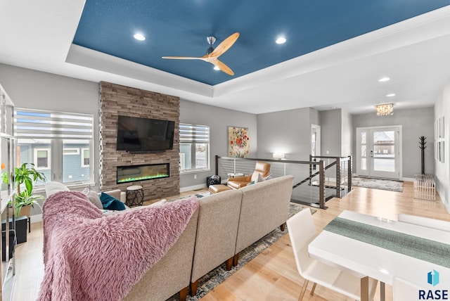 living room featuring a fireplace, a tray ceiling, a wealth of natural light, and light hardwood / wood-style floors