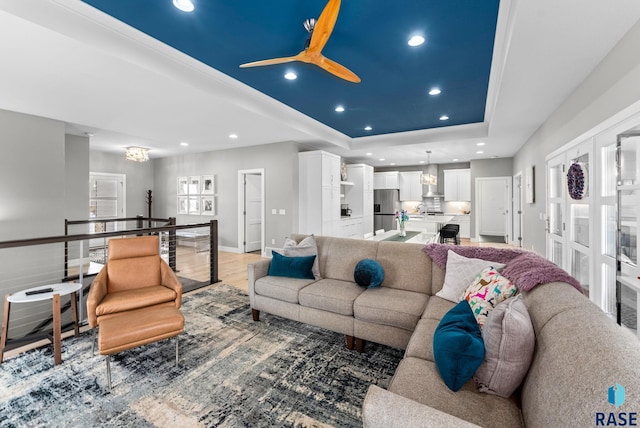 living room with an inviting chandelier, a tray ceiling, sink, and light wood-type flooring