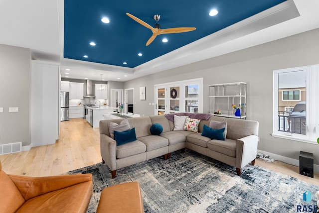 living room featuring a raised ceiling, ceiling fan, light wood-type flooring, and french doors