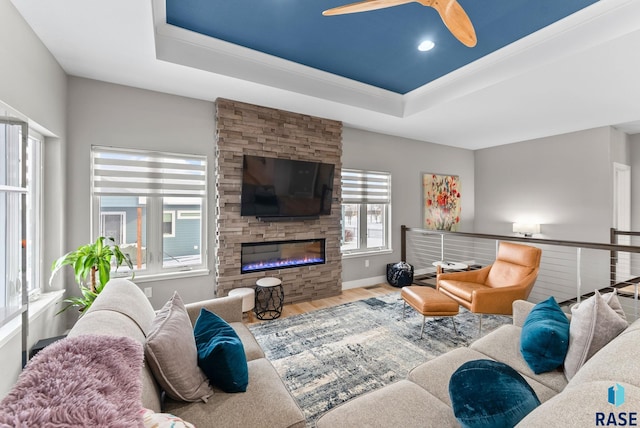 living room with hardwood / wood-style floors, a fireplace, a raised ceiling, and ceiling fan