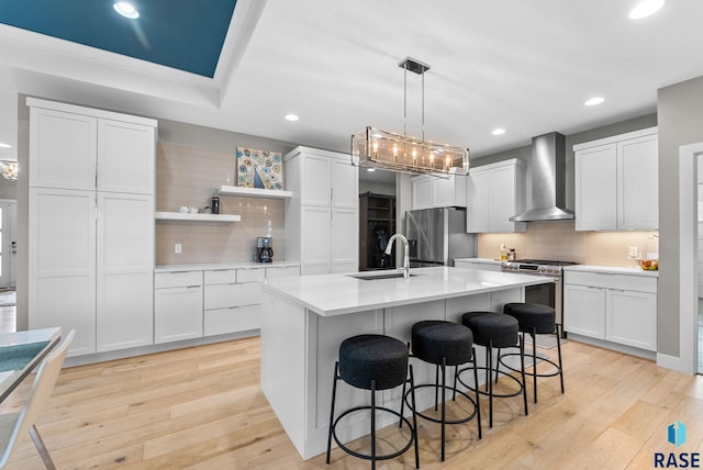 kitchen featuring sink, appliances with stainless steel finishes, white cabinets, a center island with sink, and wall chimney exhaust hood