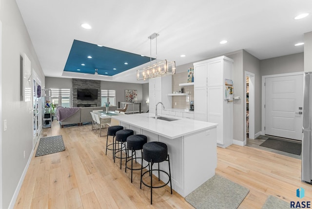 kitchen with sink, hanging light fixtures, a raised ceiling, a kitchen island with sink, and white cabinets