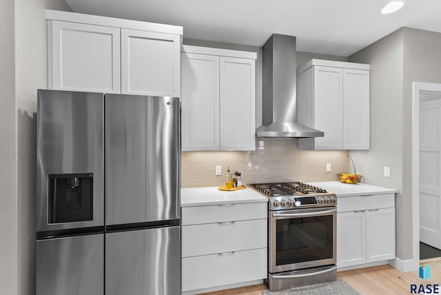 kitchen with wall chimney exhaust hood, white cabinetry, tasteful backsplash, light wood-type flooring, and stainless steel appliances