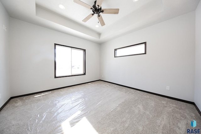 carpeted spare room featuring a raised ceiling, plenty of natural light, and ceiling fan