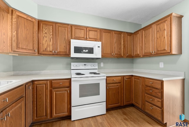 kitchen with white appliances, light hardwood / wood-style floors, and a textured ceiling