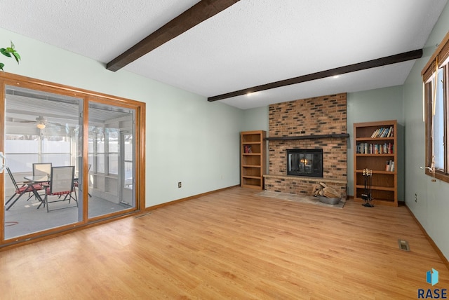 unfurnished living room with a wealth of natural light, a fireplace, beamed ceiling, a textured ceiling, and light hardwood / wood-style flooring