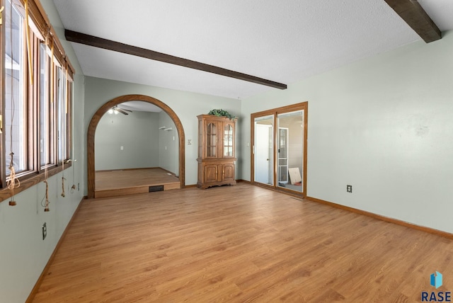 unfurnished room with beamed ceiling, a textured ceiling, and light wood-type flooring