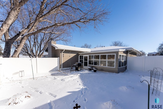 snow covered rear of property with a sunroom