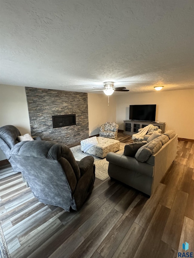 living room featuring dark hardwood / wood-style flooring, ceiling fan, a stone fireplace, and a textured ceiling