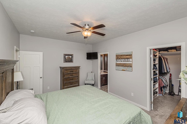 carpeted bedroom with a closet, ensuite bath, a textured ceiling, ceiling fan, and a walk in closet