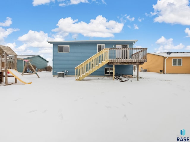 snow covered rear of property featuring a wooden deck, a playground, and central air condition unit