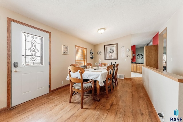 dining space featuring lofted ceiling, a textured ceiling, and light wood-type flooring