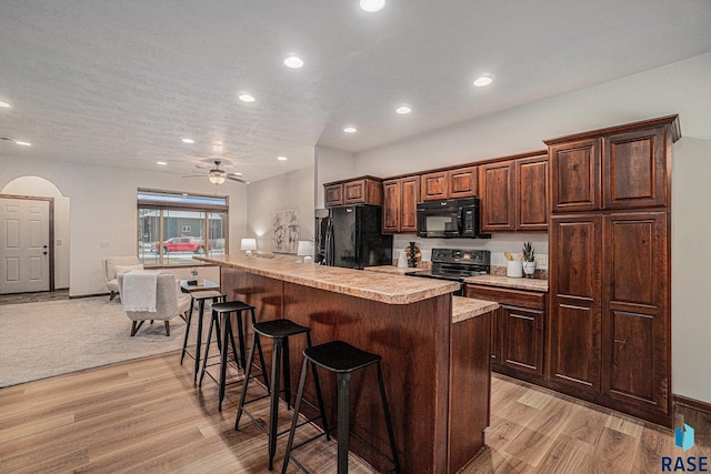 kitchen featuring a kitchen bar, a center island, black appliances, a textured ceiling, and light hardwood / wood-style flooring