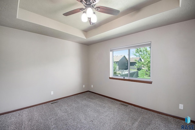 carpeted spare room with a textured ceiling, ceiling fan, and a raised ceiling