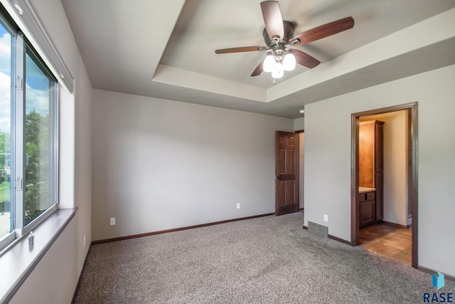 unfurnished bedroom featuring carpet, multiple windows, ensuite bath, and a raised ceiling