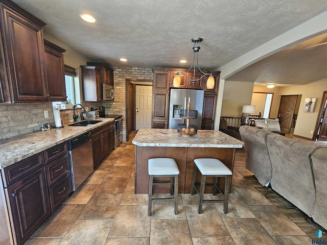 kitchen featuring tasteful backsplash, stainless steel appliances, decorative light fixtures, a kitchen island, and sink