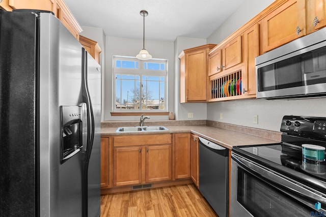 kitchen with hanging light fixtures, appliances with stainless steel finishes, sink, and light hardwood / wood-style flooring