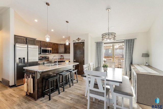 kitchen with appliances with stainless steel finishes, light hardwood / wood-style flooring, pendant lighting, and dark brown cabinets