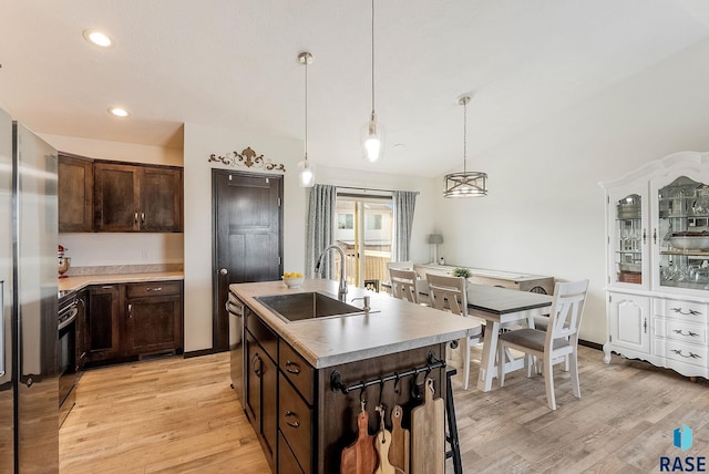 kitchen with a center island with sink, dark brown cabinets, light wood-type flooring, decorative light fixtures, and sink