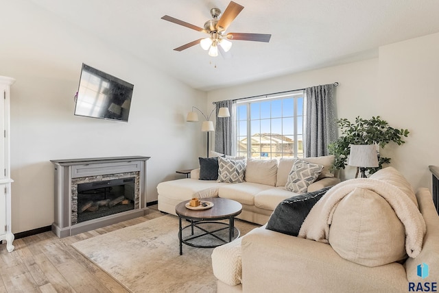 living room featuring light hardwood / wood-style flooring, ceiling fan, and a stone fireplace