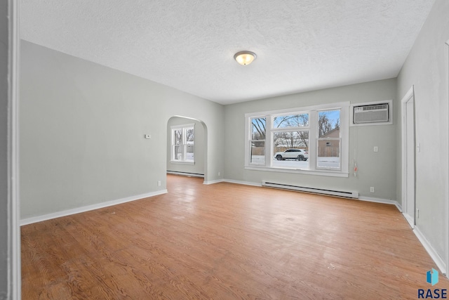 empty room with light wood-type flooring, a textured ceiling, a baseboard heating unit, and a wall unit AC