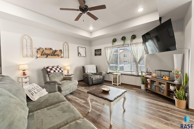 living room with hardwood / wood-style floors, ceiling fan, and a tray ceiling