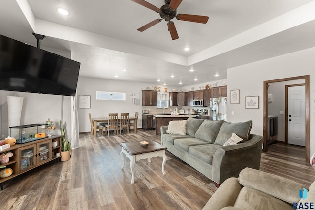 living room featuring a tray ceiling, dark wood-type flooring, and ceiling fan