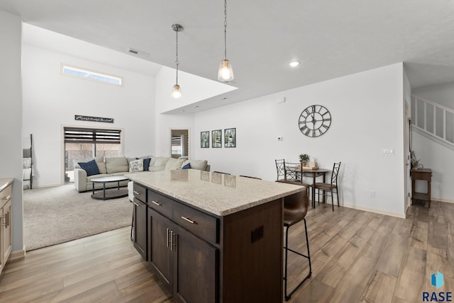 kitchen featuring a kitchen bar, light stone counters, pendant lighting, light hardwood / wood-style floors, and dark brown cabinetry