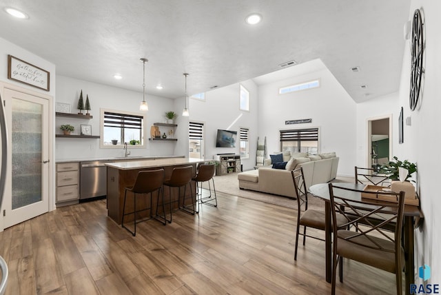 kitchen with a kitchen breakfast bar, stainless steel dishwasher, decorative light fixtures, a kitchen island, and light wood-type flooring