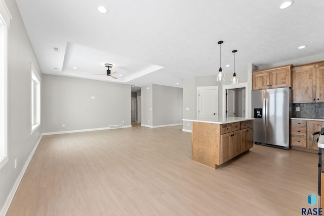 kitchen featuring pendant lighting, a raised ceiling, a kitchen island, light wood-type flooring, and stainless steel fridge with ice dispenser