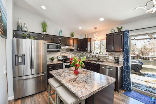 kitchen featuring hanging light fixtures, stainless steel appliances, sink, a kitchen island, and dark brown cabinetry