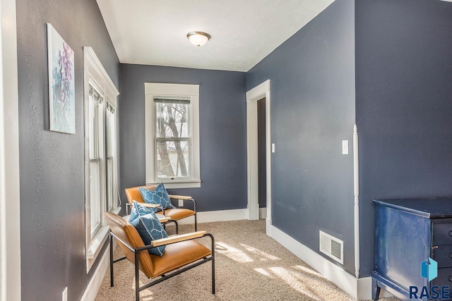 living area with baseboards, visible vents, carpet, and a textured wall