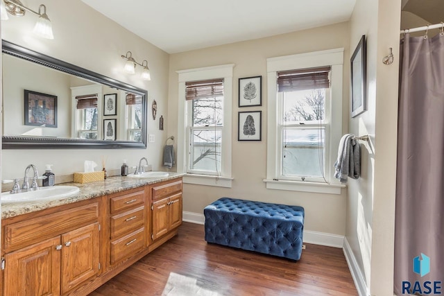 full bath with a sink, baseboards, double vanity, and wood finished floors