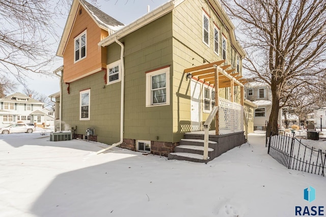 snow covered house with fence, a pergola, and cooling unit