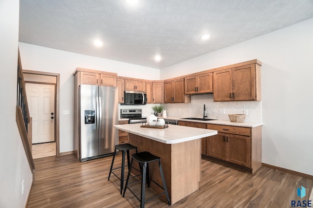 kitchen with a sink, a kitchen island, light countertops, appliances with stainless steel finishes, and a kitchen bar