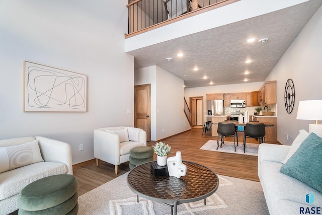 living area featuring baseboards, recessed lighting, a high ceiling, and light wood-type flooring