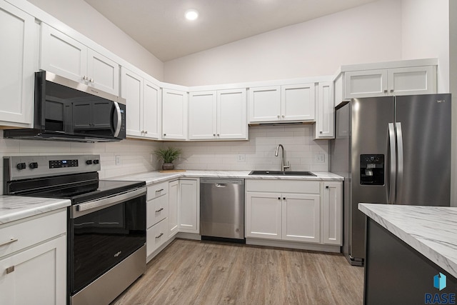 kitchen with light wood finished floors, decorative backsplash, appliances with stainless steel finishes, white cabinetry, and a sink