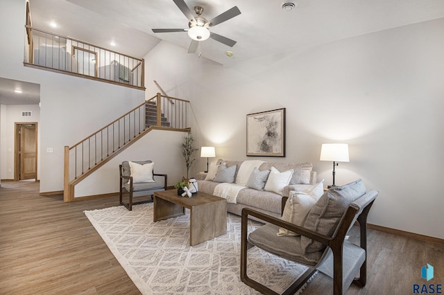 living area with wood finished floors, visible vents, a towering ceiling, stairs, and baseboards