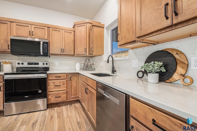 kitchen featuring light wood finished floors, stainless steel appliances, light countertops, backsplash, and a sink