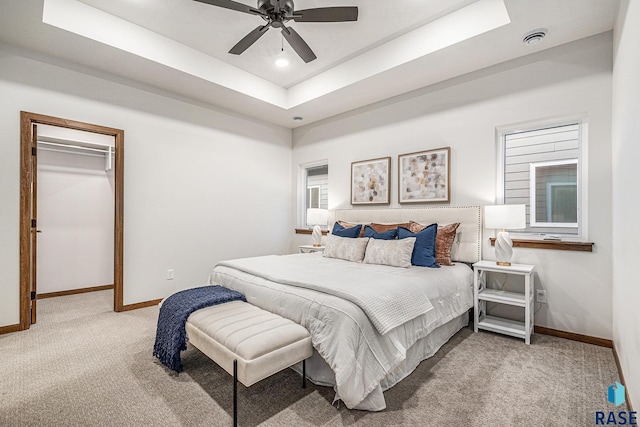 bedroom featuring a raised ceiling, light colored carpet, visible vents, a spacious closet, and baseboards