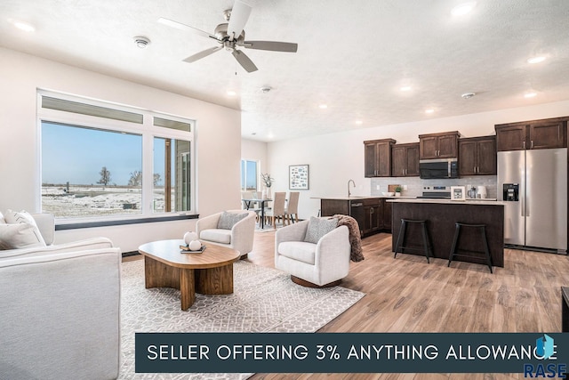 living area featuring ceiling fan, a textured ceiling, light wood-style flooring, and recessed lighting