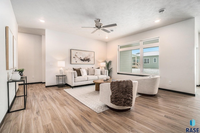 living room with a ceiling fan, baseboards, a textured ceiling, and light wood finished floors