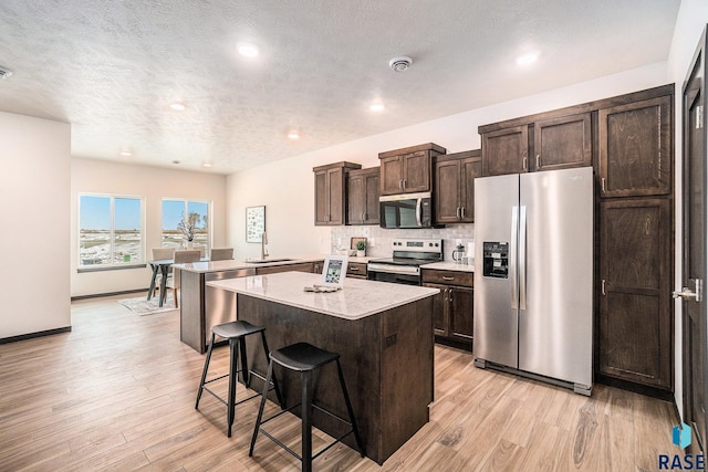 kitchen featuring light wood-style flooring, a breakfast bar area, a center island, stainless steel appliances, and a sink