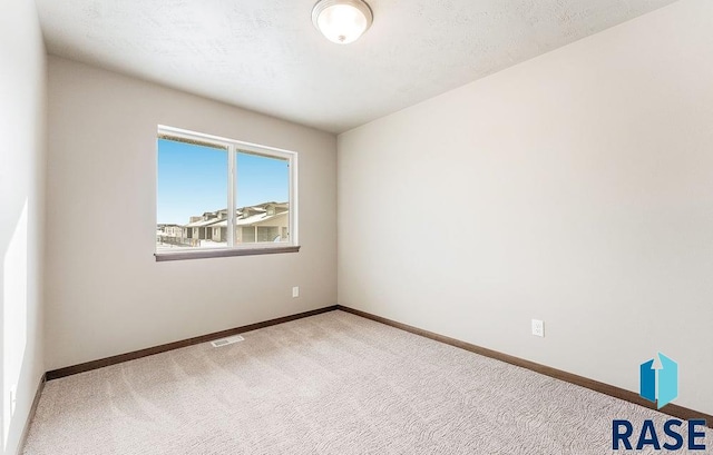 empty room featuring light colored carpet, visible vents, a textured ceiling, and baseboards