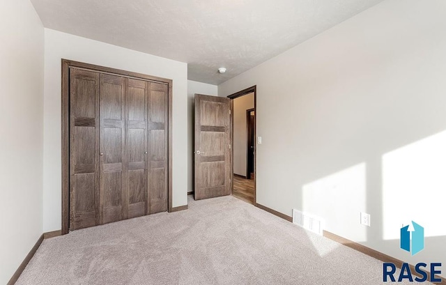 unfurnished bedroom with baseboards, a closet, visible vents, and light colored carpet