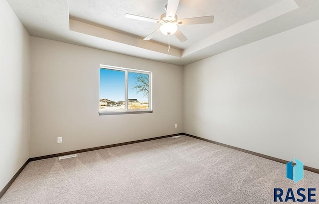 empty room featuring ceiling fan, visible vents, baseboards, a tray ceiling, and carpet