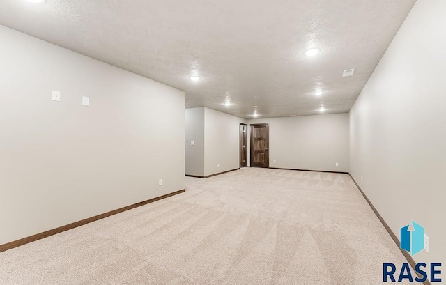 spare room featuring light carpet, baseboards, and a textured ceiling